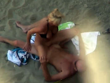Voyeur en la playa con la cámara de video graba a una pareja follando en la arena 