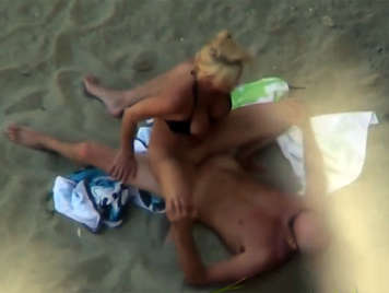 Voyeur en la playa con la cámara de video graba a una pareja follando en la arena 