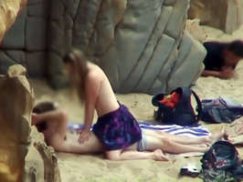 Pareja follando en la playa mientras un voyeur los obseva escondido detras de unas rocas