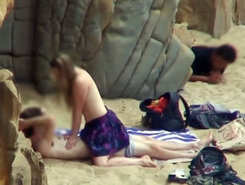 Pareja follando en la playa mientras un voyeur los obseva escondido detras de unas rocas
